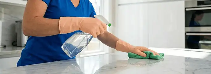 Maid service worker spraying and wiping a kitchen countertop with a microfiber cloth for sanitizing, Allentown, PA.