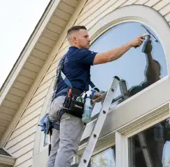 Professional window cleaner on a ladder using a squeegee to clean an exterior arched window, Allentown, PA.
