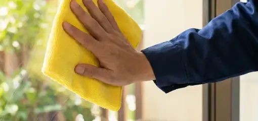 House cleaner wiping a glass window with a yellow microfiber cloth for streak-free cleaning, Allentown, PA.